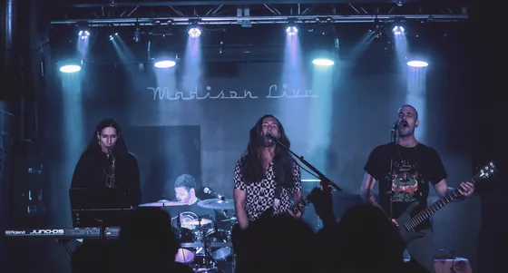 Guitar, bass and horns on a club stage under white stage lights