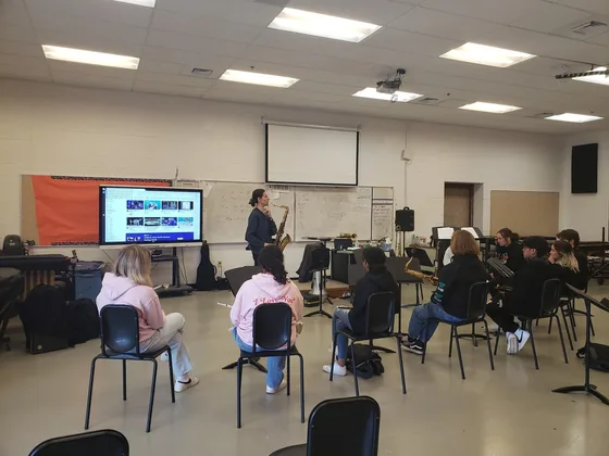 A music clinic in progress: students seated in a rehearsal room facing a screen and a presenter