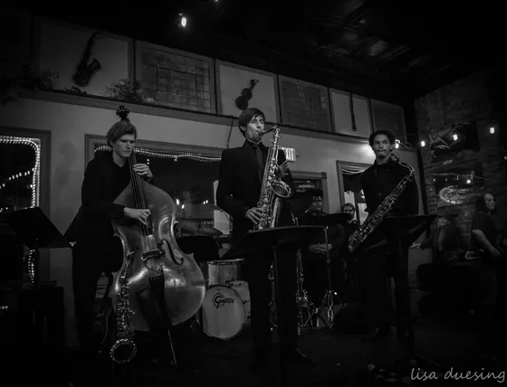 Jazz combo in black and white: upright bass, saxophone and guitar on a small stage