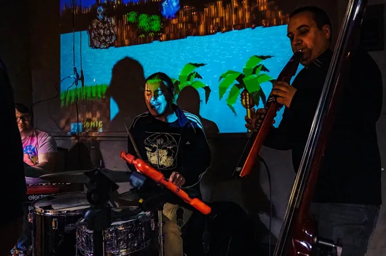 Fast Travel's bass player in front of a projected green hill level from a video game