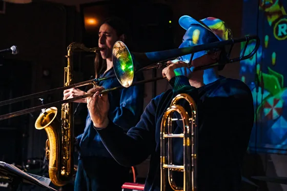 Saxophone and trombone side by side in Fast Travel's horn section under blue stage light