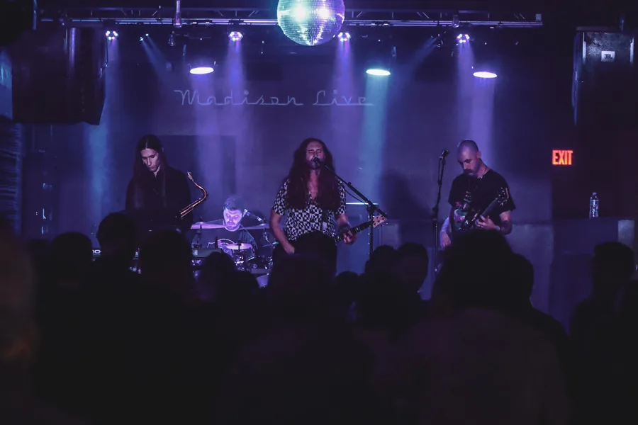 A full band on stage at Madison Live under purple lighting, mirror ball above the crowd